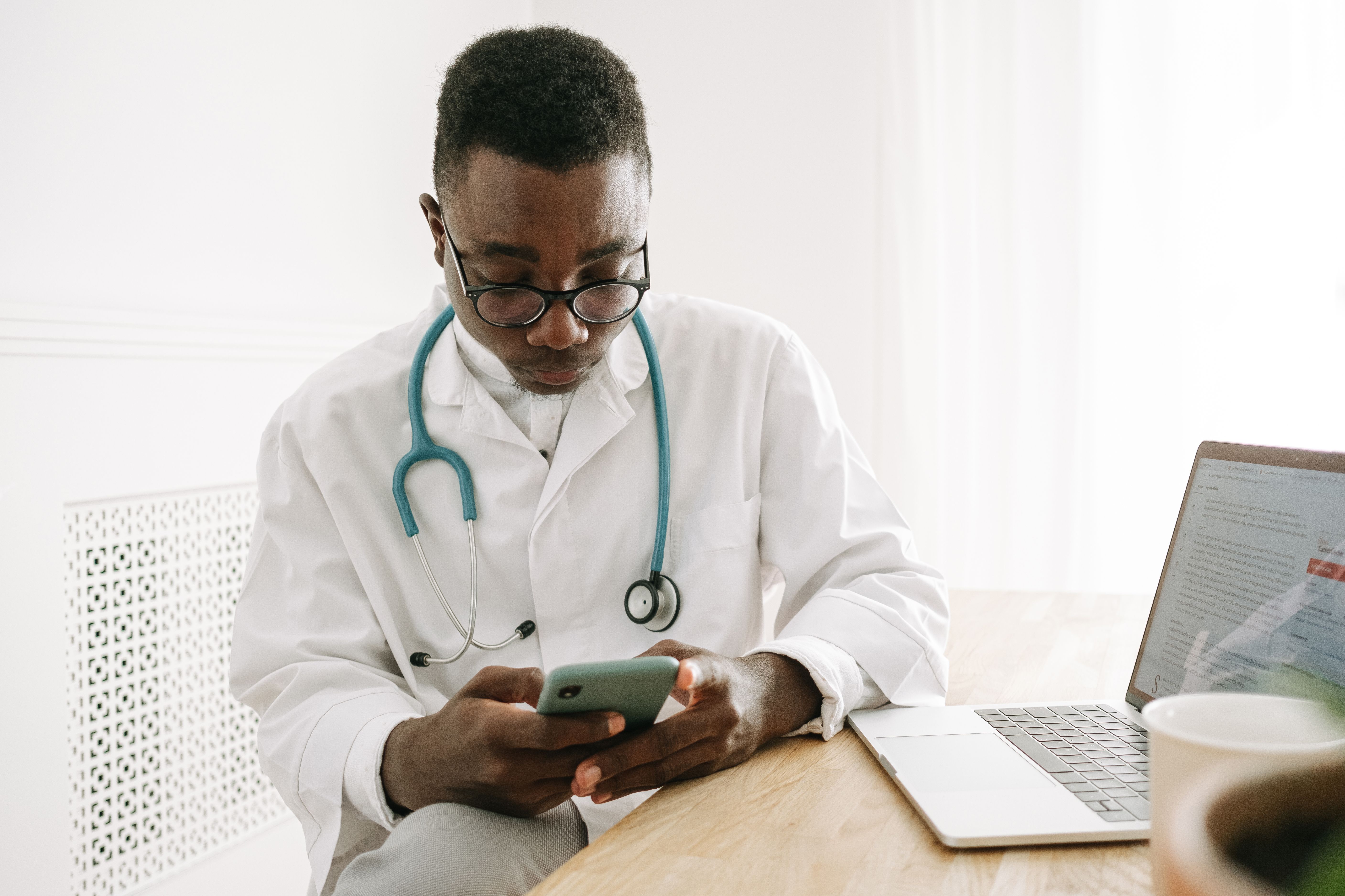 Doctor checking a smartphone beside a laptop in a medical office, representing digital health tools
