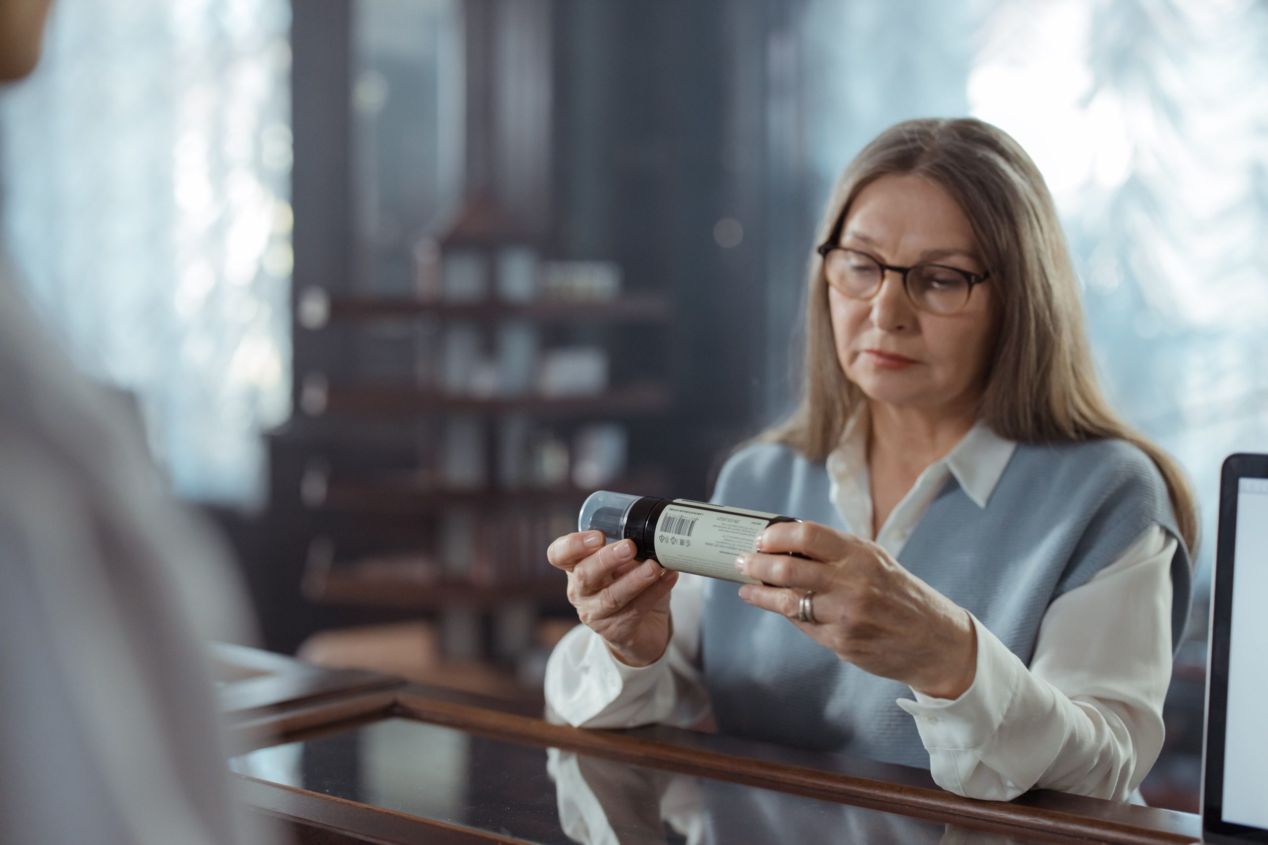 Senior woman carefully reading a medicine bottle label at a pharmacy counter